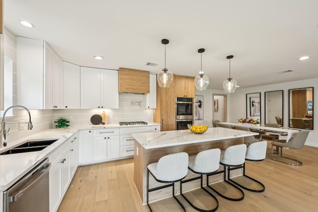 kitchen with a kitchen island, appliances with stainless steel finishes, white cabinetry, sink, and hanging light fixtures