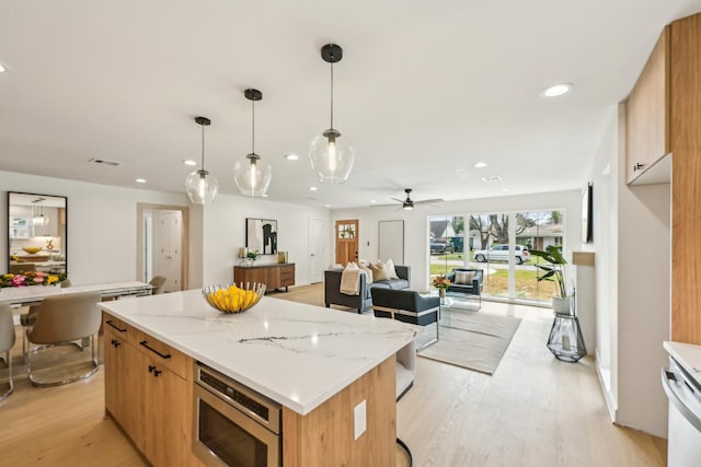 kitchen with decorative light fixtures, light hardwood / wood-style flooring, stainless steel microwave, a kitchen island, and light stone countertops