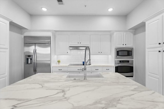 kitchen featuring light stone countertops, tasteful backsplash, white cabinetry, and built in appliances