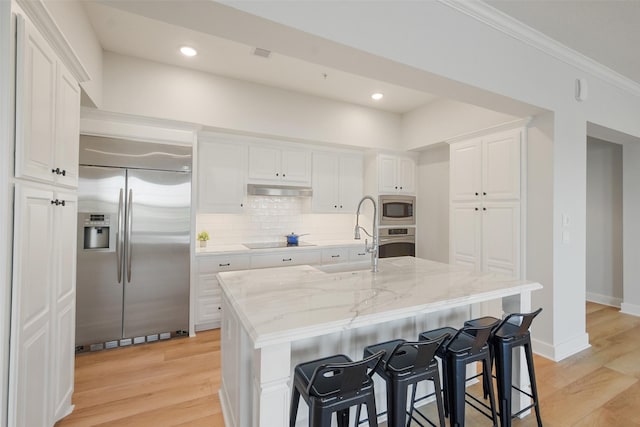 kitchen with white cabinetry, a center island with sink, a sink, and built in appliances