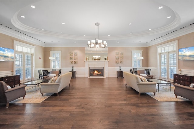 living room with a lit fireplace, a tray ceiling, dark wood finished floors, and wainscoting