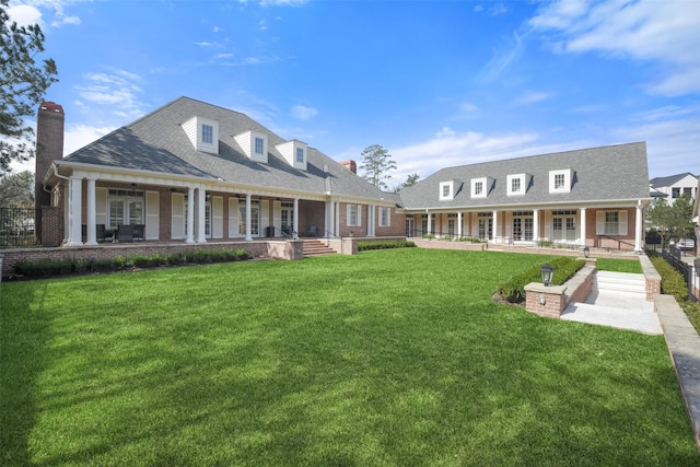 back of property featuring brick siding, a yard, a chimney, a porch, and a shingled roof