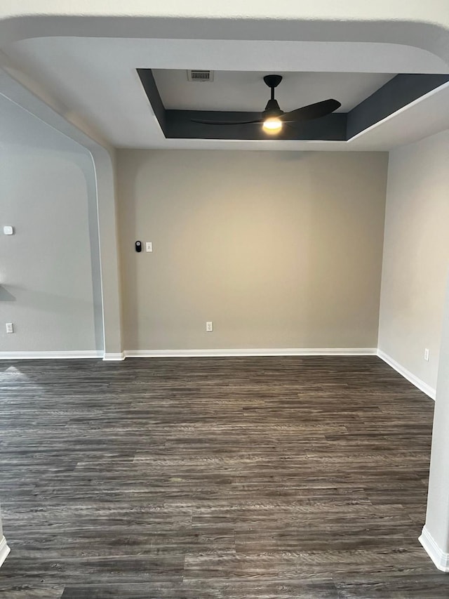 unfurnished room featuring dark wood-type flooring, ceiling fan, and a tray ceiling