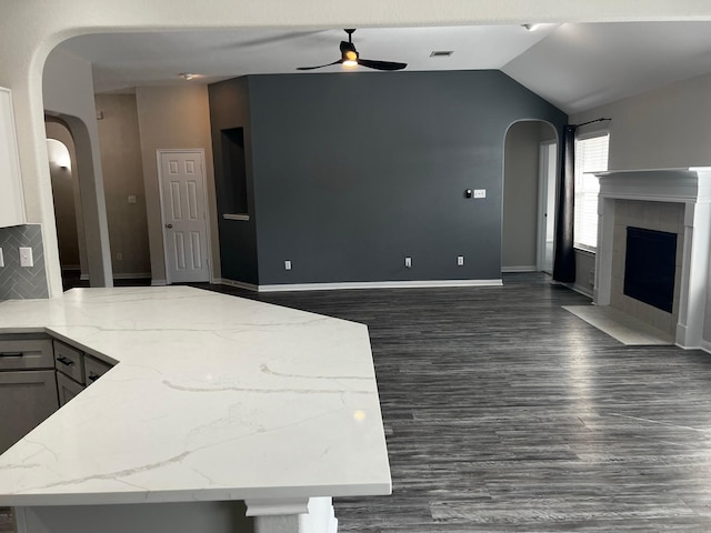 kitchen featuring lofted ceiling, dark hardwood / wood-style floors, ceiling fan, a fireplace, and backsplash