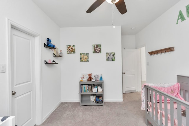 carpeted bedroom featuring ceiling fan and a crib