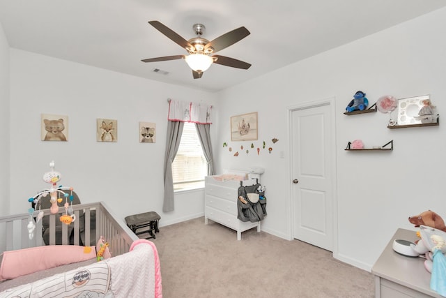 carpeted bedroom featuring ceiling fan and a crib