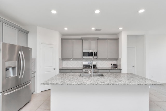 kitchen with sink, light tile patterned floors, appliances with stainless steel finishes, gray cabinets, and a kitchen island with sink