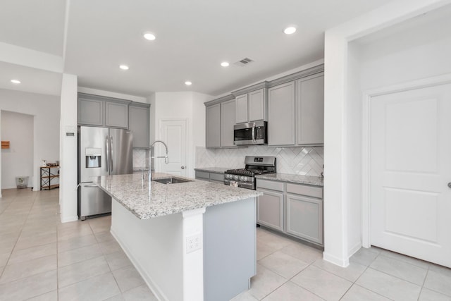 kitchen with sink, gray cabinets, a kitchen island with sink, stainless steel appliances, and light stone countertops