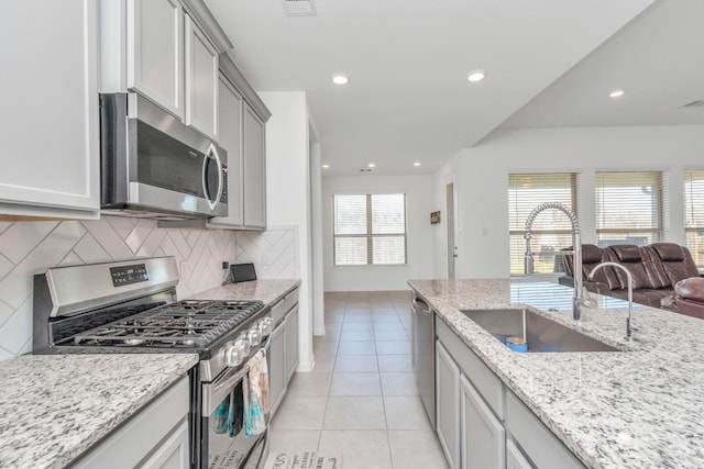 kitchen with tasteful backsplash, sink, light tile patterned floors, light stone counters, and stainless steel appliances