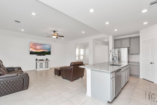 kitchen with appliances with stainless steel finishes, gray cabinetry, light stone counters, a center island with sink, and decorative backsplash