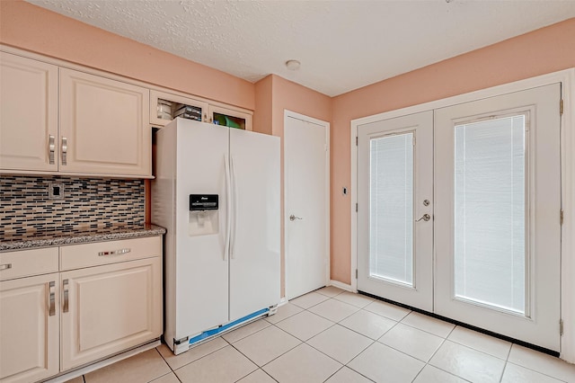 kitchen with french doors, light tile patterned floors, dark stone counters, white refrigerator with ice dispenser, and decorative backsplash