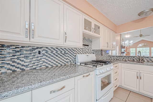 kitchen with sink, light tile patterned floors, white cabinets, vaulted ceiling, and white gas stove