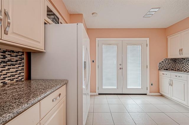 kitchen featuring backsplash, light stone counters, white fridge with ice dispenser, light tile patterned flooring, and french doors