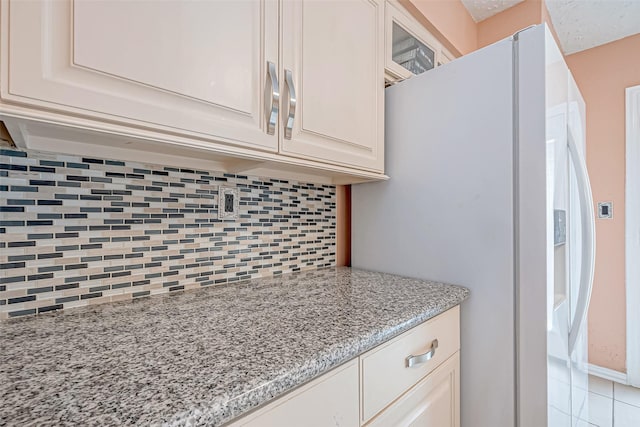 kitchen featuring light stone countertops, white refrigerator with ice dispenser, white cabinets, and decorative backsplash