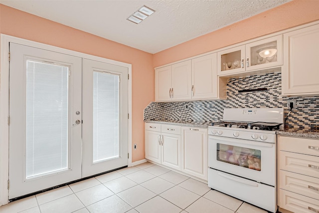 kitchen with french doors, white gas stove, white cabinetry, tasteful backsplash, and stone counters