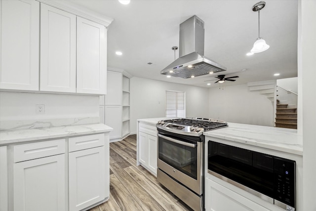 kitchen with white cabinetry, stainless steel gas range oven, built in microwave, and island range hood