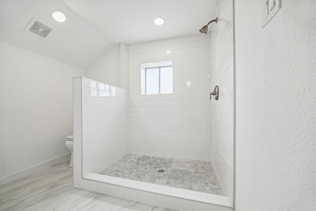 bathroom with a tile shower, vaulted ceiling, and toilet