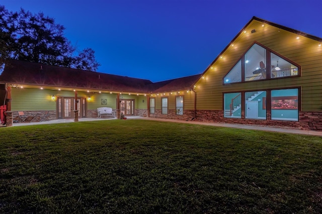 back of house at night featuring stone siding, a yard, and french doors