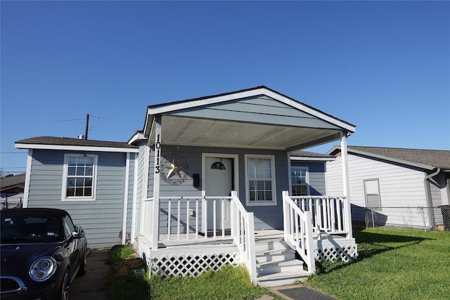 view of front facade featuring covered porch, a front lawn, and fence