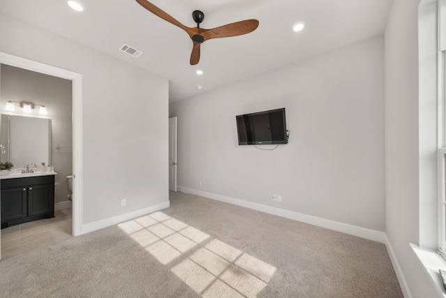 unfurnished bedroom featuring ceiling fan, light colored carpet, ensuite bathroom, and sink