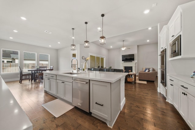 kitchen with hanging light fixtures, stainless steel appliances, an island with sink, white cabinets, and dark hardwood / wood-style flooring