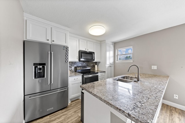 kitchen with appliances with stainless steel finishes, white cabinetry, sink, kitchen peninsula, and light hardwood / wood-style flooring