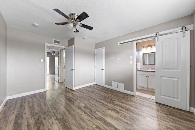 interior space with dark hardwood / wood-style floors, ceiling fan, a barn door, and a textured ceiling