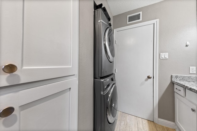 clothes washing area featuring stacked washer and dryer, a textured ceiling, and light wood-type flooring