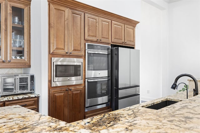 kitchen with light stone countertops, decorative backsplash, stainless steel appliances, and sink