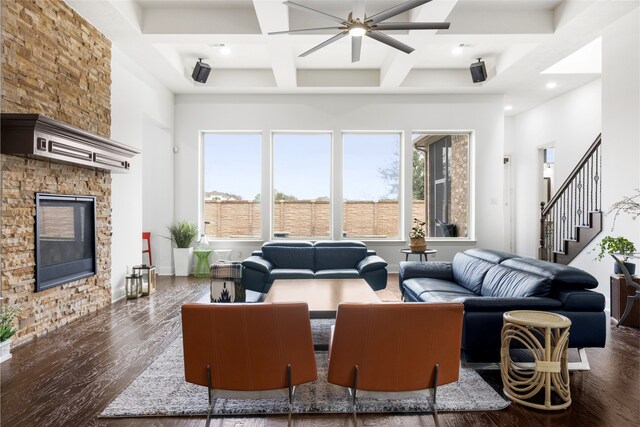 living room featuring coffered ceiling, a stone fireplace, dark hardwood / wood-style floors, ceiling fan, and beam ceiling