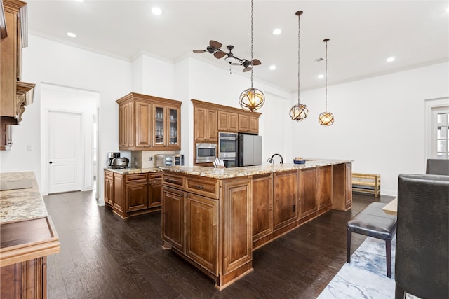 kitchen with dark wood-type flooring, light stone counters, pendant lighting, stainless steel appliances, and a kitchen island with sink