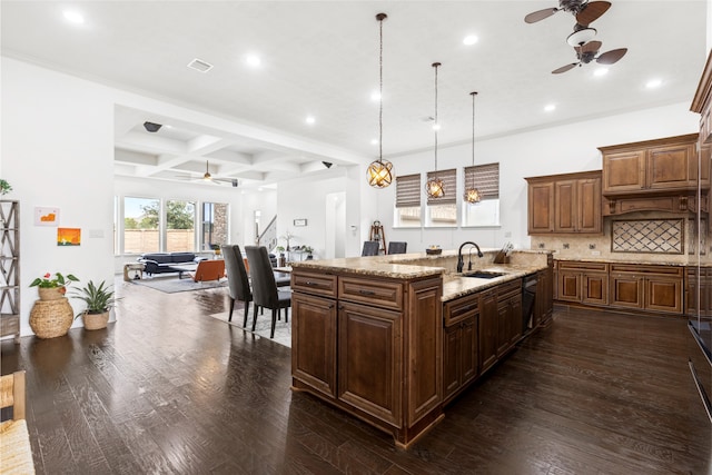 kitchen featuring hanging light fixtures, dark wood-type flooring, sink, and a center island with sink