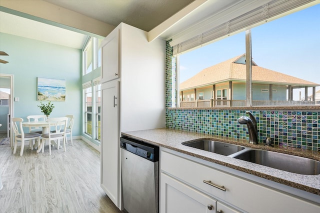 kitchen with tasteful backsplash, dishwasher, sink, white cabinets, and light hardwood / wood-style flooring