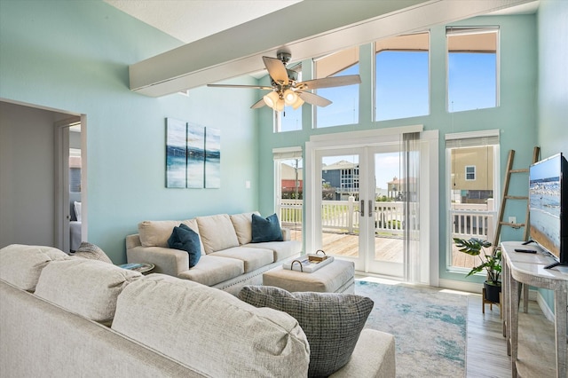 living room featuring ceiling fan, a towering ceiling, light hardwood / wood-style floors, and french doors