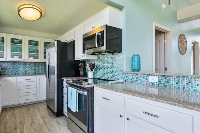 kitchen with appliances with stainless steel finishes, white cabinetry, decorative backsplash, light stone counters, and light wood-type flooring