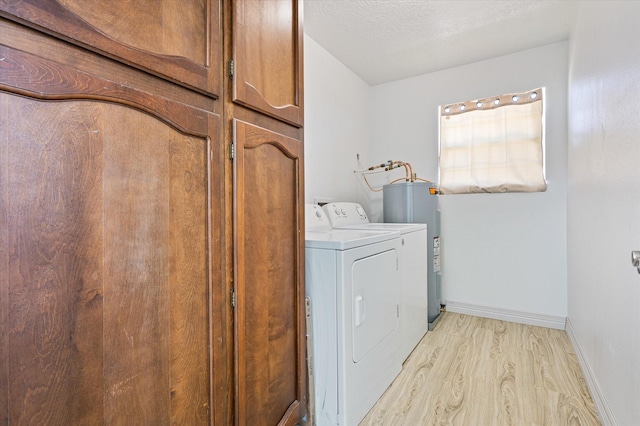 washroom featuring light hardwood / wood-style flooring, water heater, independent washer and dryer, cabinets, and a textured ceiling