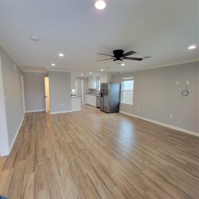 unfurnished living room with attic access, crown molding, light wood-style floors, and ceiling fan