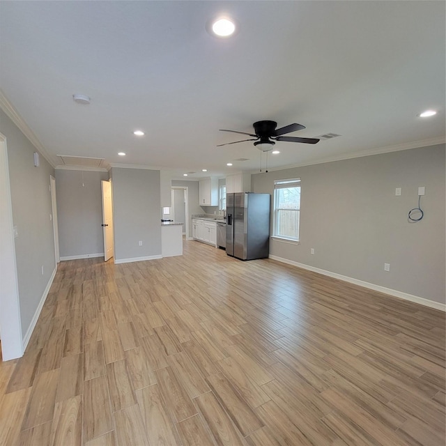 unfurnished living room with attic access, baseboards, crown molding, and light wood finished floors