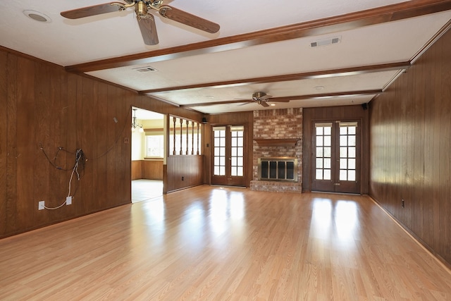 unfurnished living room featuring french doors, light hardwood / wood-style flooring, wooden walls, beamed ceiling, and a fireplace