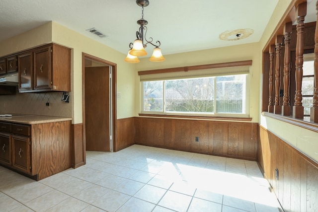 kitchen featuring pendant lighting, light tile patterned flooring, exhaust hood, and wood walls