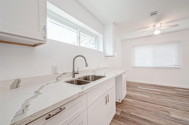 kitchen with white cabinetry, sink, ceiling fan, light hardwood / wood-style floors, and light stone countertops