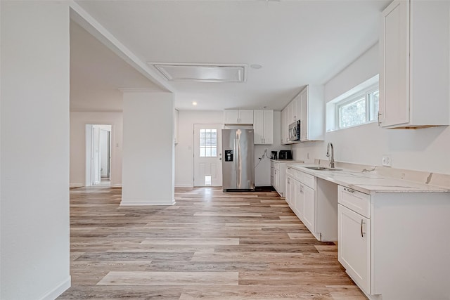 kitchen with sink, light hardwood / wood-style flooring, stainless steel appliances, light stone countertops, and white cabinets