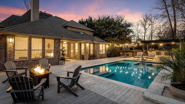 pool at dusk with a wooden deck and a fire pit