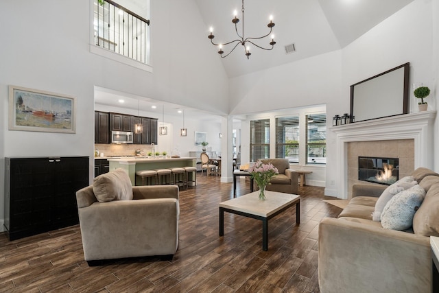 living room featuring hardwood / wood-style floors, a tile fireplace, a chandelier, and a high ceiling