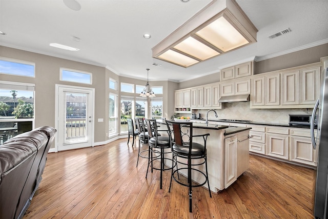 kitchen with hanging light fixtures, a center island with sink, ornamental molding, stainless steel fridge, and cream cabinets