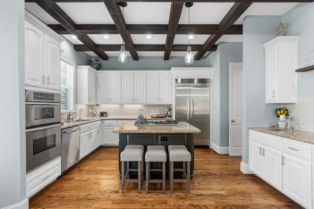 kitchen with light stone countertops, a kitchen island, white cabinets, and appliances with stainless steel finishes