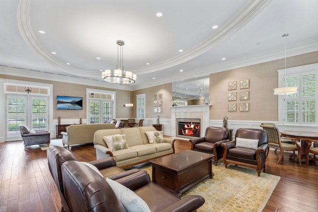 living room with hardwood / wood-style flooring, a high end fireplace, a tray ceiling, and a notable chandelier