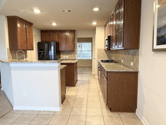 kitchen featuring light stone counters, visible vents, light tile patterned flooring, a sink, and black appliances