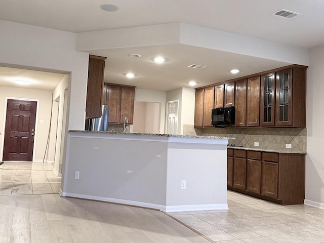 kitchen with stainless steel fridge, light hardwood / wood-style floors, light stone countertops, decorative backsplash, and kitchen peninsula