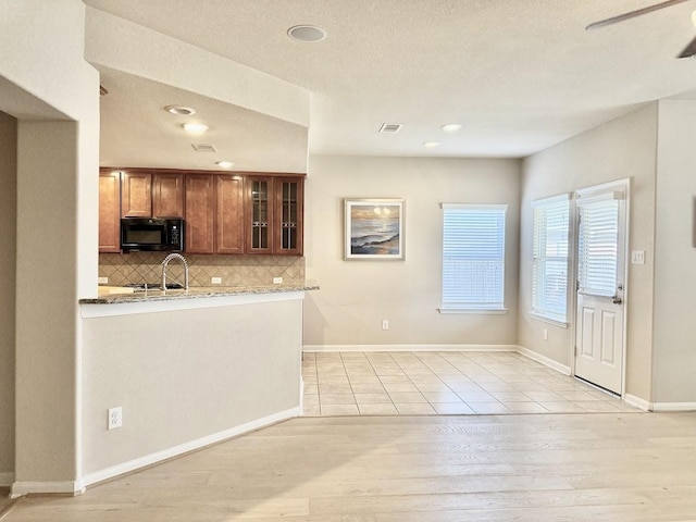 kitchen featuring visible vents, glass insert cabinets, brown cabinets, black microwave, and backsplash